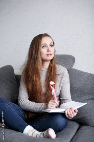Creative pensive young female sitting on the couch at home writing something in Poster Mural XXL