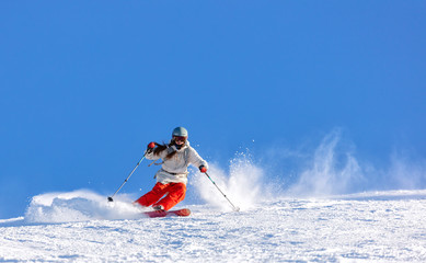 Girl On the Ski. a skier in a bright suit and outfit with long pigtails on her head rides on the track with swirls of fresh snow. Active winter holidays, skiing downhill in sunny day. Woman skier