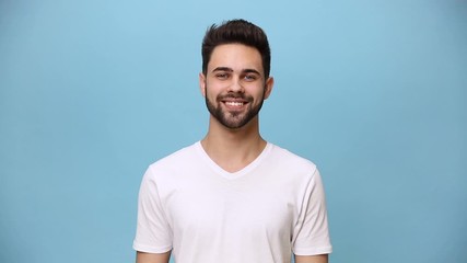 Wall Mural - Handsome unshaven bearded young guy 20s wearing white t-shirt isolated over pastel blue background in studio. People sincere emotions lifestyle concept. Looking in different sides directions smiling