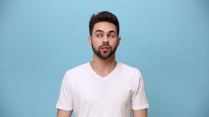 Wall Mural - Handsome unshaven bearded young guy 20s wearing white t-shirt isolated on pastel blue background in studio. People sincere emotions lifestyle concept. Looking in different sides directions suspicious