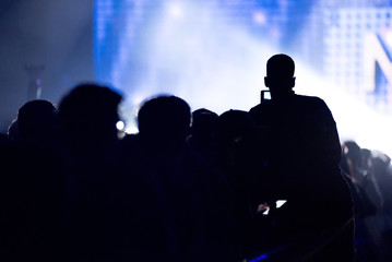 Wall Mural - Silhouette of raised hands holding a smart phone recording music concert