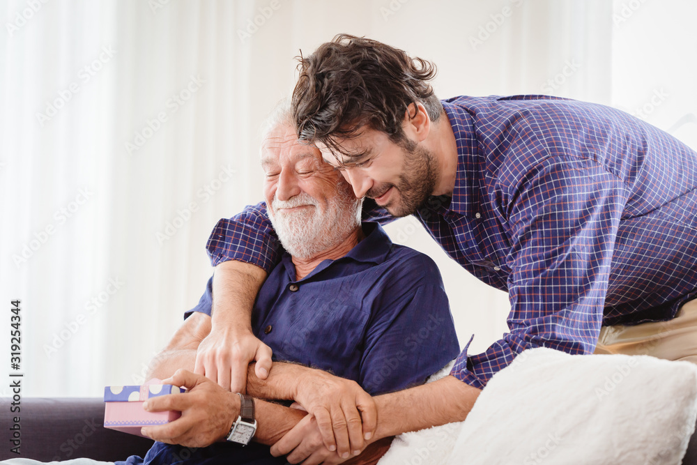 young man hugs the uncle old man warmly inside the house, son happy and love his father or grand father with gift box concept - obrazy, fototapety, plakaty 