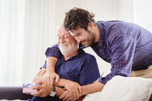 Young Man Hugs The Uncle Old Man Warmly Inside The House, Son Happy And Love His Father Or Grand Father With Gift Box Concept