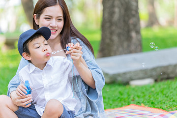 Beautiful mother playing with her son enjoy holiday outdoor green park background.