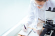 © Quality Stock Arts - Scientist doctor taking note or writing memo on working day in virus research with microscope in hospital medical lab