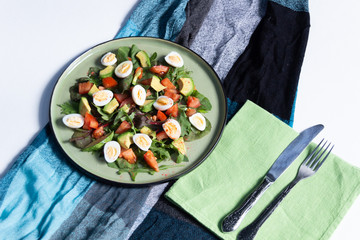 Canvas Print - fresh salad with green leaves, eggs, tomato, avocado in a plaate on textile cover and fork with knife  on white background