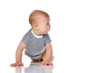 Infant child boy in t-shirt and green pants is crawling on all fours, looking aside at free copy space reading on white