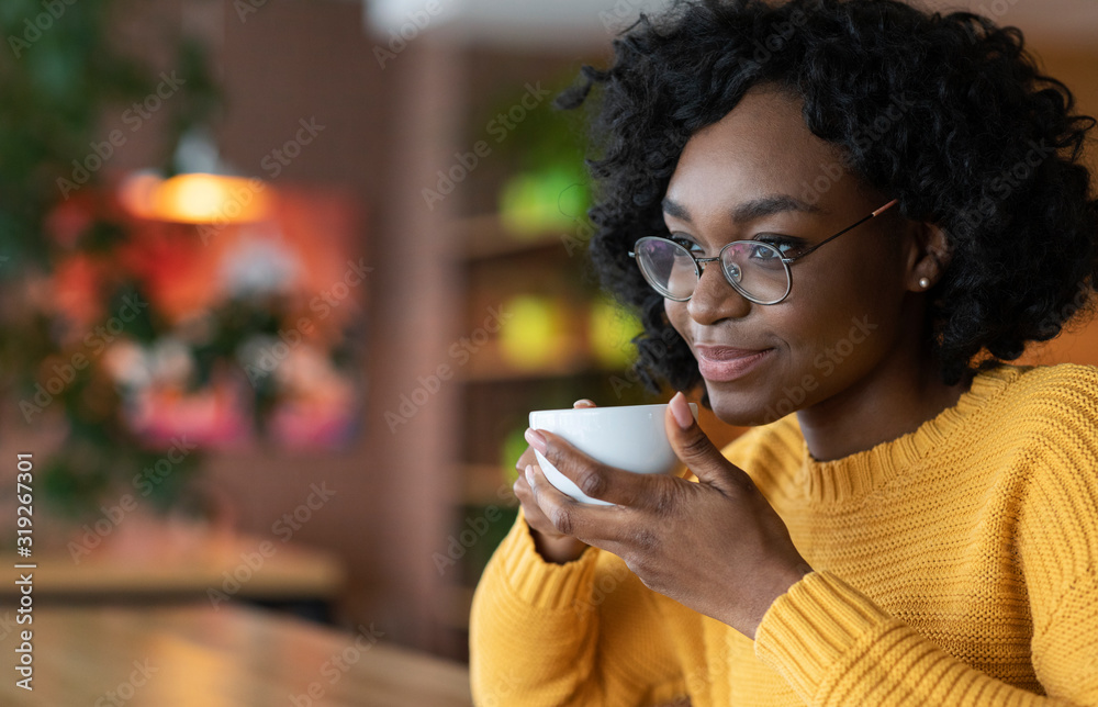 Dreamy young black lady enjoying cup of coffee in cafe - obrazy, fototapety, plakaty 