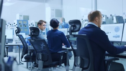 Modern Factory: Female Project Supervisor Talks to a Male Industrial Engineer who Works on Computer. They use CAD Software for Design, Development. In Background High-Tech Industrial Equipment
