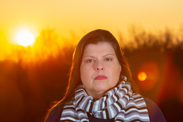 Wall Mural - Lady outdoor closeup portrait  during a beautiful cold colorful winter sunset. She is serious, looking at the camera and wearing season clothes.