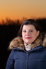 Wall Mural - Lady outdoor closeup portrait  during a beautiful cold colorful winter sunset. She is showing a little smile and looking at the camera. She is wearing season clothes.