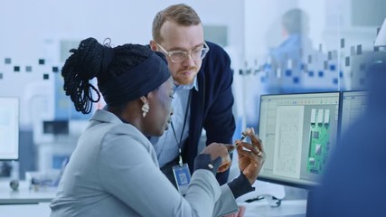 Wall Mural - Modern Electronics Factory: Female Supervisor Talks to a Male Electrical Engineer who Works on Computer with CAD Software. Designing PCB, Microchips, Semiconductors and Telecommunications Equipment