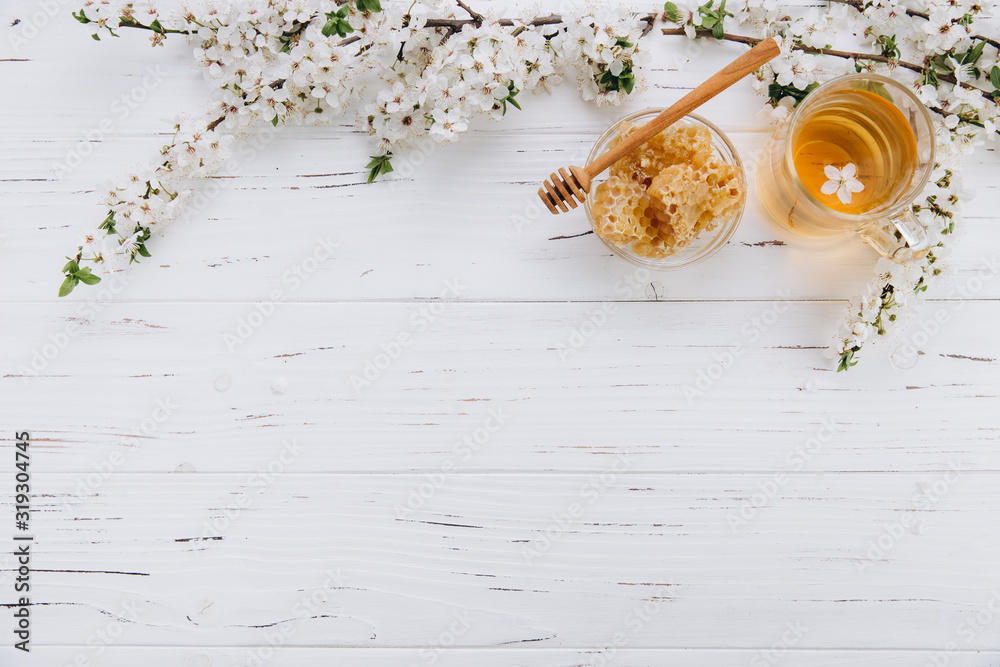 Spring composition. A cup of herbal tea and a jar of honey on a white wooden background, cherry flowers top view. Place for text. Healthy food concept. - obrazy, fototapety, plakaty 