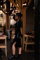 Photo of brunette lady posing on wooden background in cafe.Fashion style portrait. Girl wearing dark casual dress, sunglasses and dark hat .Fashion concept.