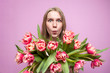 © Богдан Маліцький - emotional face of a girl in flowers on a pink background, a surprised woman with a bouquet of tulips is smiling