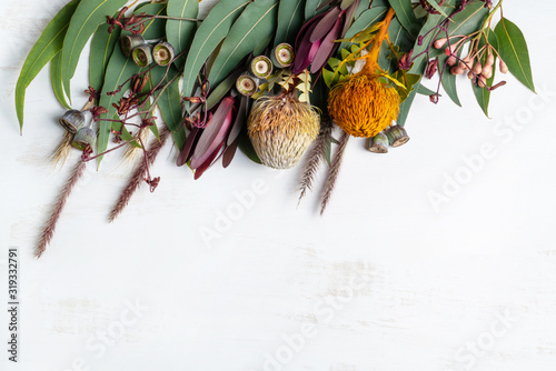 Beautiful flat lay floral arrangement of mostly Australian native flowers, including Protea, Banksia, Kangaroo paw; Eucalyptus leaves and Gum nuts on a white background.
