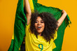 © Brastock Images - Afro girl cheering for favorite brazilian team, holding national flag in yellow background.