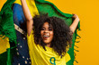 © Brastock Images - Afro girl cheering for favorite brazilian team, holding national flag in yellow background.