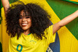 © Brastock Images - Afro girl cheering for favorite brazilian team, holding national flag in yellow background.