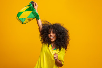 Brazil supporter. Brazilian woman fan celebrating on soccer or football match on yellow background. Brazil colors.