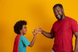 © Nexa - African Father and Son playing Superhero at the day time. People having fun yellow background. Concept of friendly family.