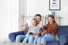 Young Family Playing Video Games While Sitting On Sofa At Home