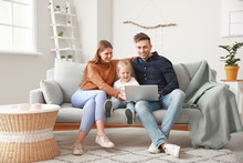Happy Young Family With Laptop Sitting On Sofa At Home
