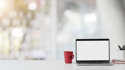 Closeup view of office room with blank screen laptop, stationery, coffee cup and copy space on white table