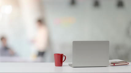 Close up view of workspace with laptop, notebooks, red coffee cup and copy space on white desk