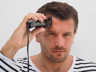 Man cutting his own hair with a clipper. Lifestyle.