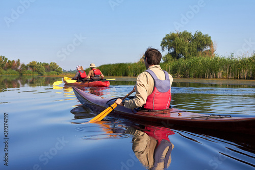 Fotomural Rear view of man paddling the wooden kayak and couple in red kayak kayaking in t