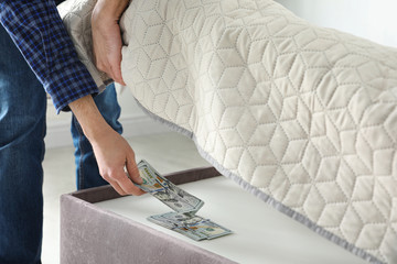 Man hiding dollar banknotes under mattress in bedroom, closeup. Money savings