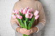 Woman with beautiful pink spring tulips near white brick wall, closeup