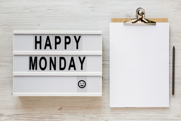 'happy monday' words on a modern board, clipboard with blank sheet of paper on a white wooden surfac