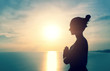 Woman meditating with namaste hands in the bright sunset light on the sea background, view from the side