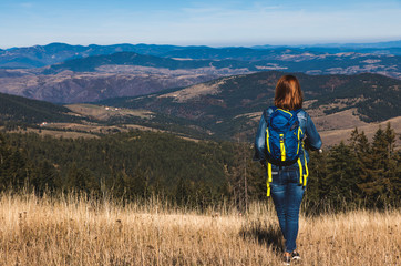 Wall Mural - rear view of female hiker with backpack standing on top of the mountain enjoying the view during the