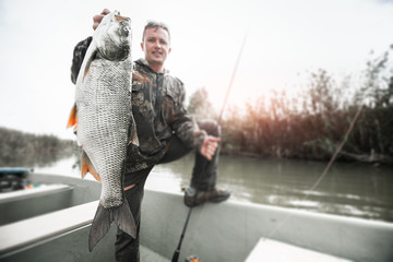 Wall Mural - Amateur angler stands in the boat and holds the trophy Asp fish (Leuciscus aspius) with natural background. Tilt shift effect applied, image is blurred, focus on the fish only.