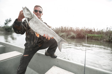 Wall Mural - Amateur angler stands in the boat and holds the Asp fish