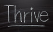 The word Thrive written by hand in white chalk on a blackboard as a reminder