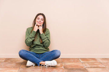 Young caucasian woman sitting on the floor isolated doubting between two options.