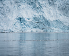 Close Up shot of huge Glacier wall. Large chunks of ice breaking off. Moody and overcast weather. Eqip Sermia Glacier called Eqi Glacier. Greenlandic ice cap melting because of global warming.