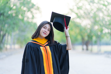 Portrait of a young cheerful female graduate wearing academic gown holding graduate cap celebrate her university degree in commence day in college campus.