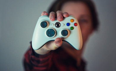 Close up of teenage boy hand showing a gamepad console for playing video games. Man holding joystick isolated on grey wall background with copy space. Marketing presentation, virtual world controller.