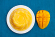Mango pudding, jelly, dessert on white plate. Blue textile background. Top view.