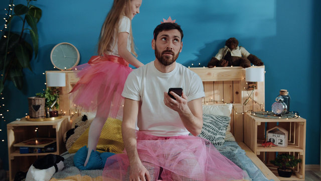 portrait of tired bored young man in fairy dress using a smartphone sitting on bed. happy princess g