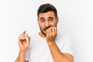 Wall Mural - Young caucasian man holding a thermometer isolated Young caucasian man holding  a biting fingernails, nervous and very anxious.