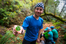 A Man Stands On A Trail Smiling Holding A Four-leaf Clover While Backpacking The Lost Coast Trail In Sinkyone Wilderness State Park In Northern California.