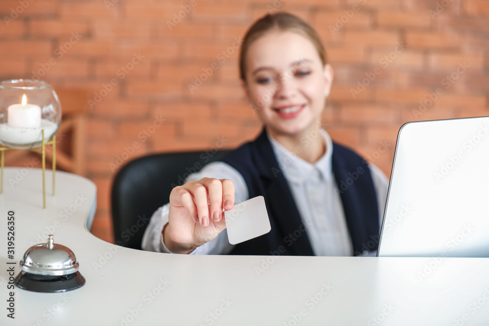 Young female receptionist with card at desk in hotel