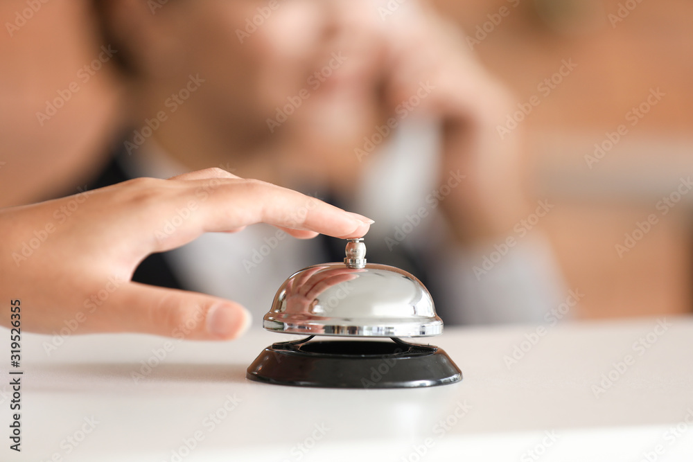 Woman ringing service bell on reception desk in hotel, closeup