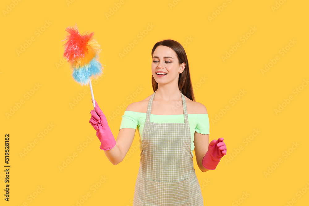Young housewife with dust brush on color background